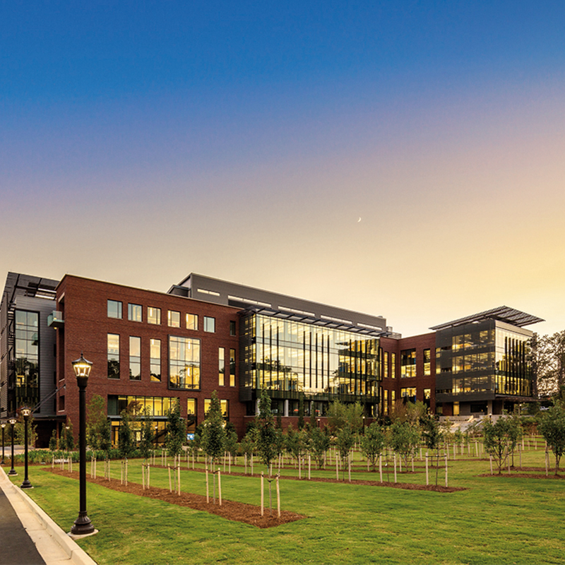 A modern brick-and-glass research building overlooking a landscaped lawn at sunset.