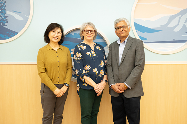 Three adults stand side by side in front of a wall with circular landscape artwork, posing for a group photo.